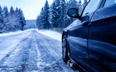 Black car on an iced road surrounded by trees covered with snow A black car on an iced road surrounded by trees covered with snow