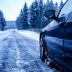 A black car on an iced road surrounded by trees covered with snow