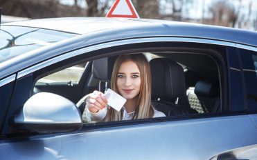 Joyful girl driving a training car with a drivers license card in her hands.