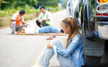 A young woman sits crying next to the car she crashed into someone on the road. A young woman sits crying next to the car she crashed into someone on the road.
